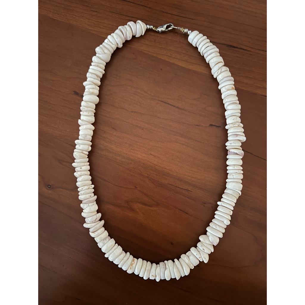 Vintage Hawaiian puka shell necklace of chunky irregular white shell chips strung on a cord, photographed flat on a wooden surface